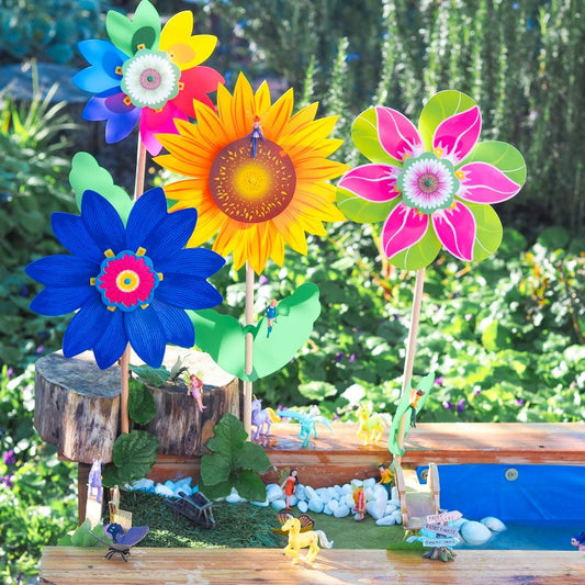 Colorful flower-shaped wind spinners in a garden setting with small figurines and a wooden bench.